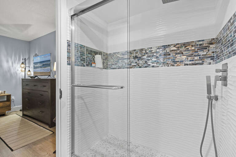 A stylish walk-in shower featuring textured white tiles, beautiful blue mosaic accents, and a sleek glass door, providing a refreshing and modern bathing experience.