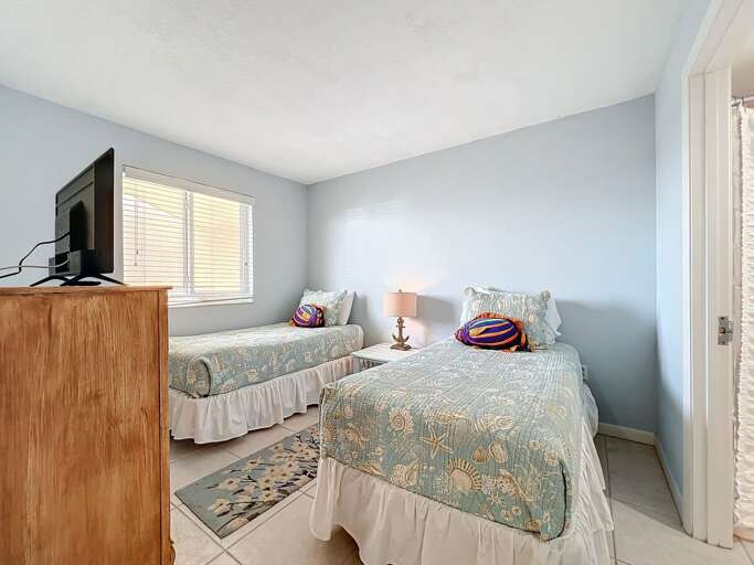 This charming twin bedroom features nautical-themed bedding, a flat-screen TV, and ample natural light, creating a relaxing retreat for guests.