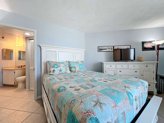 Retreat to this coastal-themed bedroom featuring a comfortable bed, ample storage, a flat-screen TV, and an en-suite bathroom for added convenience.