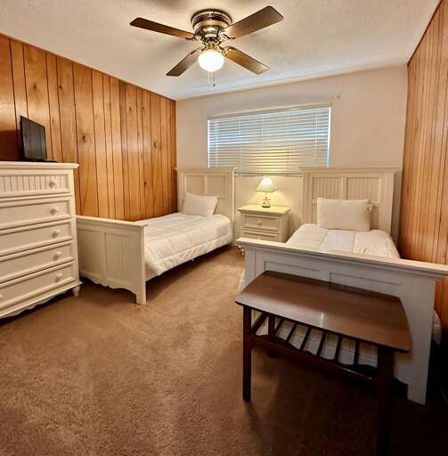 Charming bedroom with two twin beds, cozy white linens, and classic wood-paneled walls. A central Charming bedroom with two twin beds, cozy white linens, and classic wood-paneled walls. A central