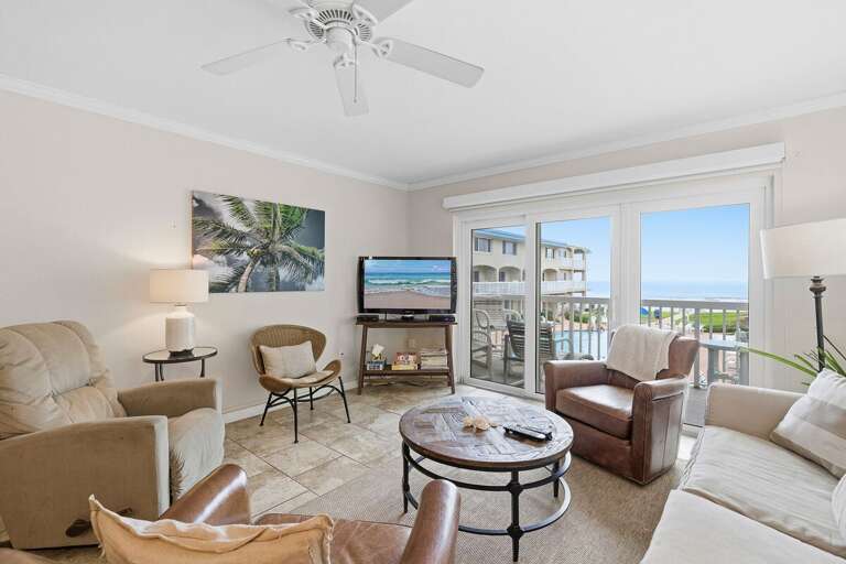 Relax in this bright coastal living room featuring comfortable seating, beach-inspired décor, and balcony access with ocean views overlooking the pool. A perfect beach stay for your seaside getaway.