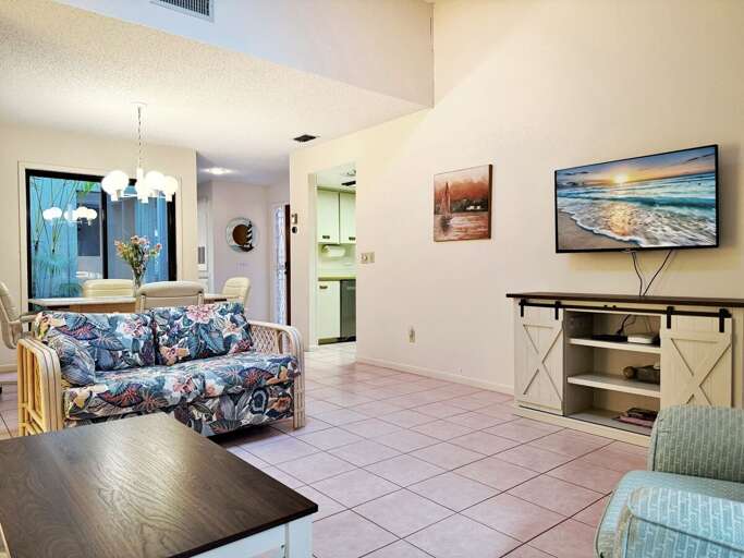 Relax in this inviting beach condo living space featuring coastal décor, a comfy floral sofa, flat-screen TV, and a dining area—perfect for unwinding after sun-filled days by the shore. Relax in this inviting beach condo living space featuring coastal décor, a comfy floral sofa, flat-screen TV, and a dining area—perfect for unwinding after sun-filled days by the shore.