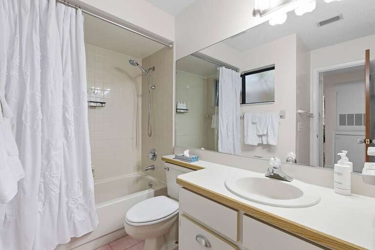 This bright guest bathroom features a tub-shower combo, large vanity, and fresh coastal touches. A