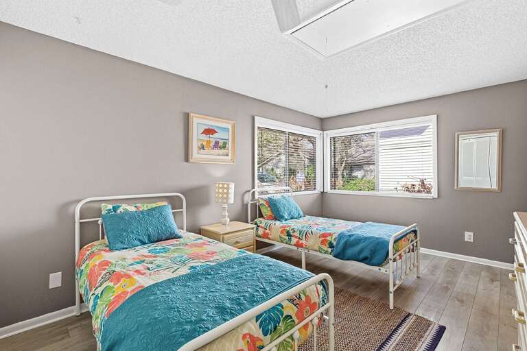 This bright twin bedroom features colorful coastal décor, comfy beds, and sunny windows—perfect