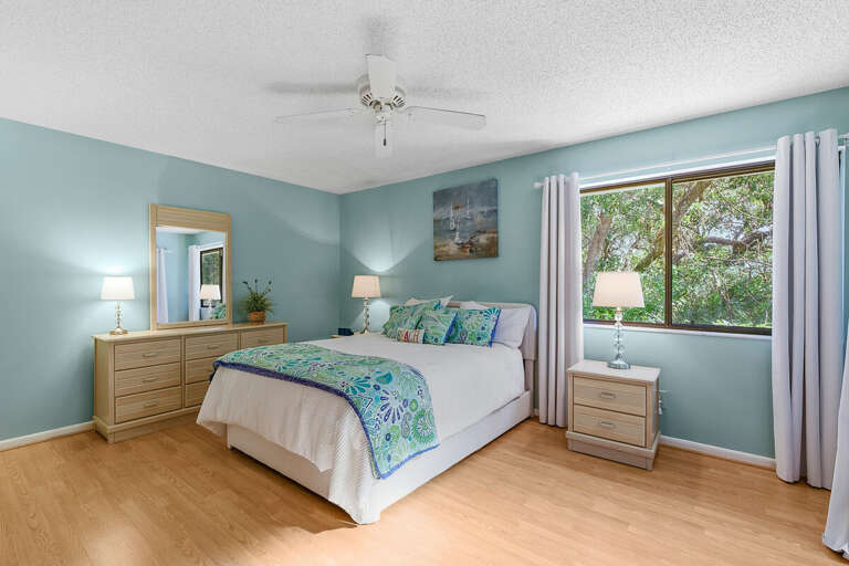 Rest easy in this spacious coastal bedroom featuring a plush bed, soothing beach-inspired décor,