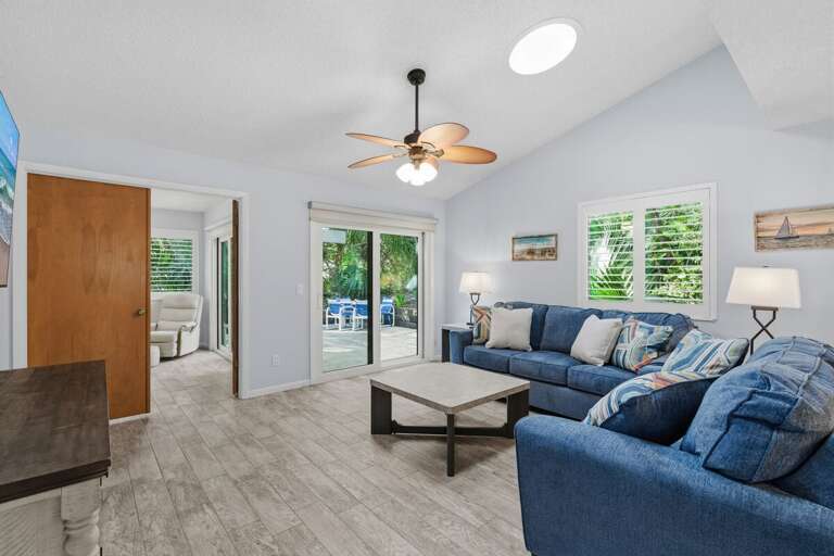 Spacious Living Space With Sleek Sofa, Shaded Windows, And Sliding Door Leading To Light-filled Locale