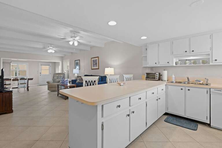 Spacious Kitchen Flowing Into Living Area With White Cabinets And Island