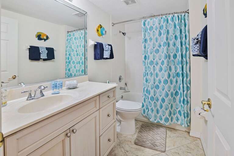 Fresh and inviting, this beach-themed bathroom features a shower/tub combo, bright ocean-blue accents, and ample counter space—perfect for rinsing off after a day by the shore.