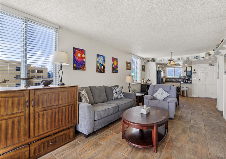 Enjoy a spacious living room with plush seating, coastal décor, and natural light. The open layout flows seamlessly into the kitchen and dining area, creating the perfect setup for your beach stay