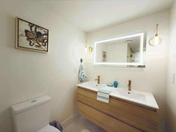 Enjoy a fresh coastal feel in this modern bathroom featuring a sleek double vanity, illuminated mirror, and stylish décor—perfect for unwinding after a sun-soaked beach day.