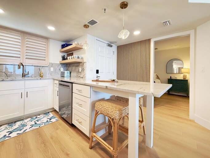 Enjoy a beach getaway with this open, modern kitchen featuring marble counters, stylish shelving, and a cozy breakfast bar—perfect for morning coffee before hitting the sand.