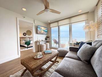 Relax in this bright, coastal-inspired living room featuring ocean views, cozy seating, and access to a private balcony—perfect for morning coffee or sunset lounging during your beach getaway.