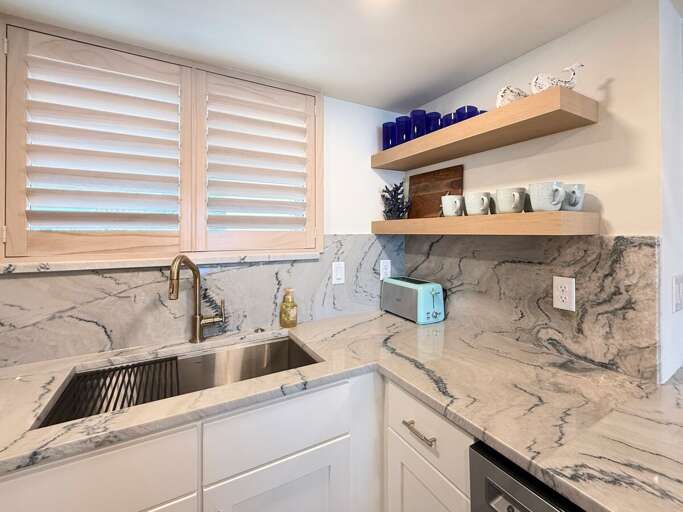 This stylish kitchen features marble countertops, open shelving, and a deep farmhouse sink—perfect for creating meals and enjoying your relaxing beach getaway in comfort.
