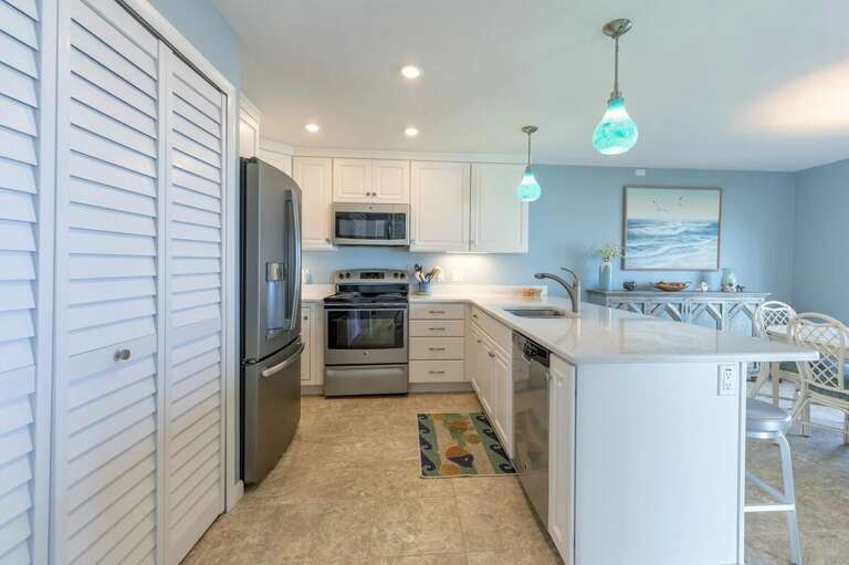 Cook with ease in this fully equipped kitchen featuring stainless steel appliances, bright coastal décor, and a spacious breakfast bar—perfect for beach vacation meals and family gatherings.