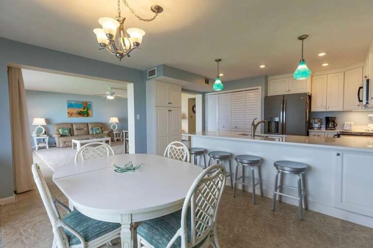Gather with family in this bright beach condo featuring a spacious dining area, modern kitchen with breakfast bar seating, and coastal décor—perfect for relaxing after a day by the ocean.