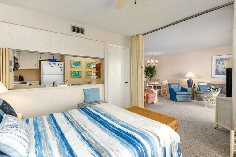 This beach stay suite offers a cozy bedroom with ocean-hued bedding, an open pass-through kitchenette, and direct access to a spacious living and dining area for a relaxed seaside retreat. This beach stay suite offers a cozy bedroom with ocean-hued bedding, an open pass-through kitchenette, and direct access to a spacious living and dining area for a relaxed seaside retreat.