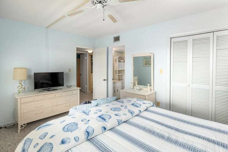 Unwind during your beach stay in this airy bedroom, featuring seashell-themed bedding, ample storage, a flat-screen TV, and easy access to the bathroom for a comfortable seaside retreat. Unwind during your beach stay in this airy bedroom, featuring seashell-themed bedding, ample storage, a flat-screen TV, and easy access to the bathroom for a comfortable seaside retreat.