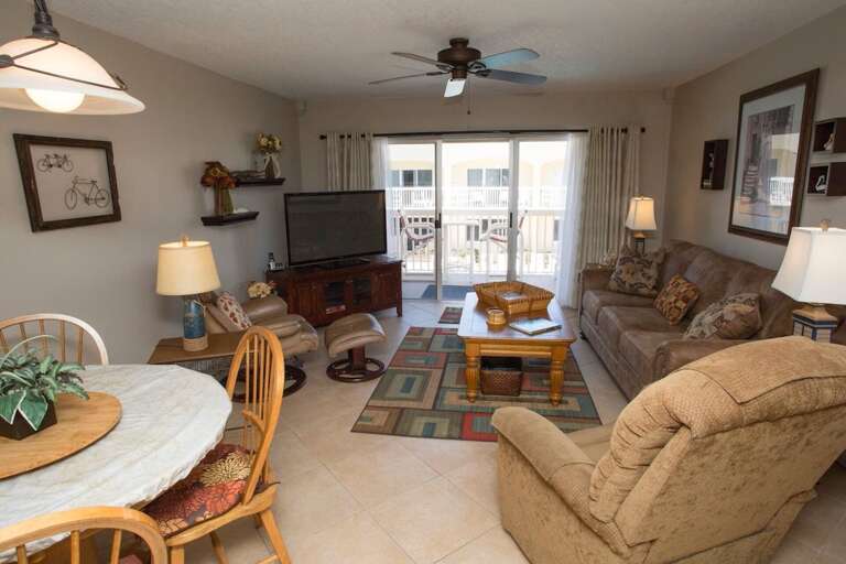 Relax in this inviting living room with plush seating, flat-screen TV, and natural light from sliding doors leading to the balcony—perfect for unwinding after a fun-filled beach day. Relax in this inviting living room with plush seating, flat-screen TV, and natural light from sliding doors leading to the balcony—perfect for unwinding after a fun-filled beach day.