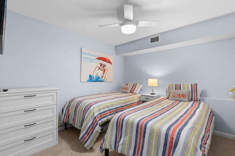 This bright beach-themed bedroom with twin beds and playful coastal décor is perfect for kids or friends to relax after a fun-filled day by the ocean.