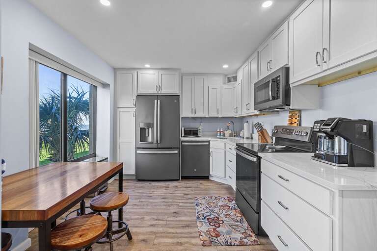 Cook up seaside favorites in this modern, fully equipped kitchen featuring stainless steel appliances, sleek white cabinetry, and a cozy breakfast nook with a view—perfect for your beach getaway.