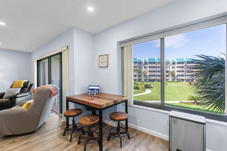 Enjoy breakfast with a view in this cozy beach condo dining nook overlooking lush resort grounds and palm trees. Perfect for a relaxed start before heading to the sand and surf.
