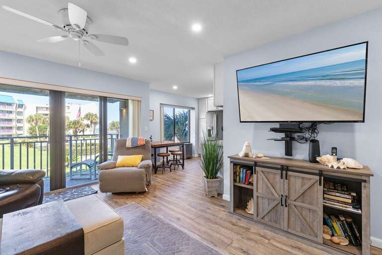 Enjoy coastal comfort in this inviting beach condo featuring a large TV, cozy seating, and balcony access with scenic resort and ocean views—perfect for a relaxing seaside escape.