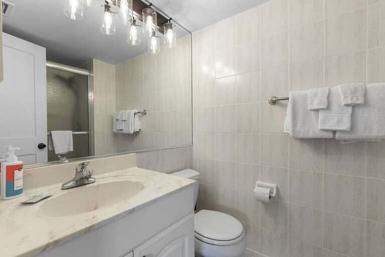 Freshen up after a day at the beach in this clean, modern bathroom featuring bright lighting, soft towels, and a walk-in shower—perfect for unwinding after your seaside adventures.