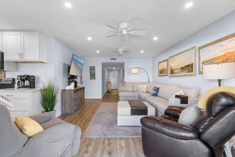 Unwind in this airy coastal living space featuring plush seating, beach décor, and an open layout that flows into the kitchen—perfect for relaxing after a day of seaside adventures.