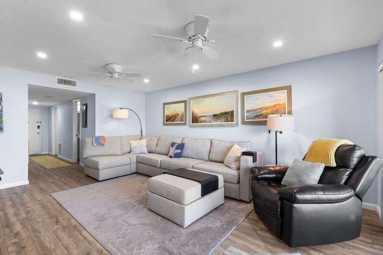 Unwind in this bright, beach-inspired living room featuring cozy seating, coastal artwork, and soft tones—perfect for relaxing after a day of sun, sand, and surf during your seaside getaway.