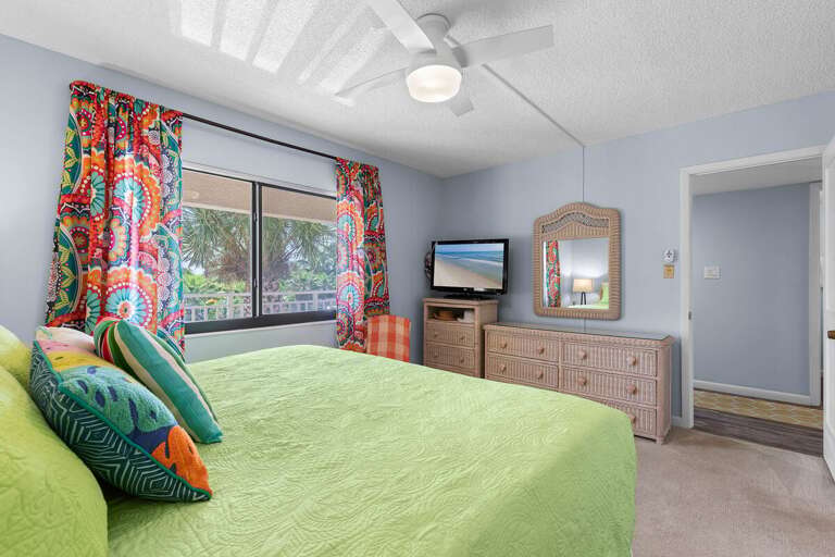 Wake up to island vibes in this bright, beach-inspired bedroom featuring tropical décor, a flat-screen TV, and lush palm views—perfect for relaxing after sun-soaked adventures by the shore.