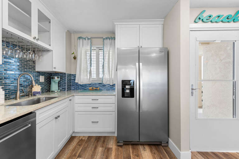 Stylish beach-inspired kitchen with stainless appliances, ocean-blue backsplash, and natural light—perfect for preparing meals during your relaxing seaside getaway.