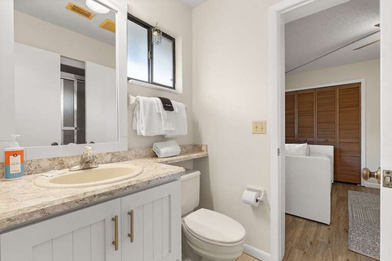 Freshen up after a beach day in this clean, coastal-style bathroom featuring soft lighting, plush towels, and a bright, inviting atmosphere for your seaside getaway.