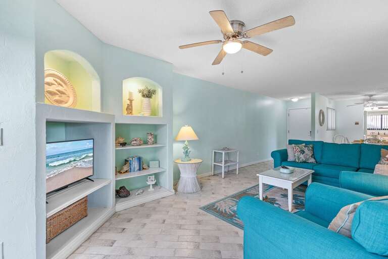Relax in this coastal-style living room featuring ocean-inspired décor, built-in shelving, and a flat-screen TV — the perfect spot to enjoy your beach getaway in comfort and style.
