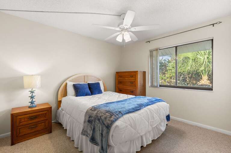 Rest easy in this serene beach-inspired bedroom featuring cozy bedding, warm natural light, and lush garden views — a perfect retreat after a day by the ocean.
