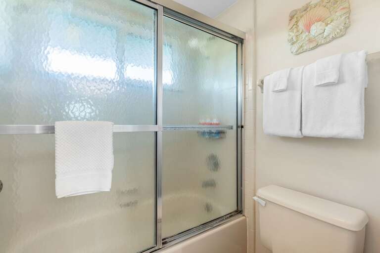 Rinse off after the beach in this bright, coastal-style bathroom featuring a glass-enclosed shower and fresh towels — perfect for unwinding after a day of sun and sea.