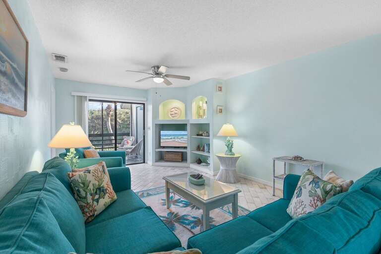 Soak in the seaside atmosphere from this cozy beach-themed living room featuring ocean décor, a flat-screen TV, and patio access for the perfect coastal retreat experience.