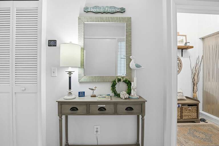 Charming beach stay accent area with coastal decor, mirror, and stylish console table. Welcoming touches create a relaxed beach house vibe, perfect for setting the tone for your seaside getaway.