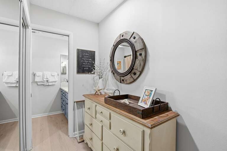 Inviting beach stay hallway leading to the bedroom and bath, featuring coastal decor, a stylish dresser, and nautical accents. A bright, welcoming space that enhances your relaxing beach getaway.