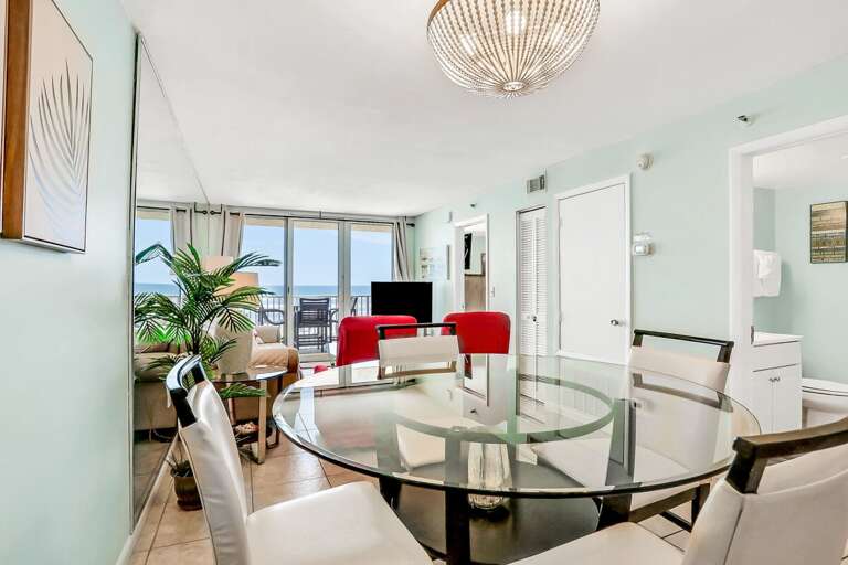 Bright Beachside Vacation Rental With Glass Dining Table And Red Chairs, Opening To A Balcony