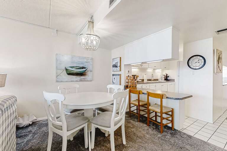 White-walled Dining Space With Chic Chandelier Above Round Table, Leading Into Kitchen With Bar Stools