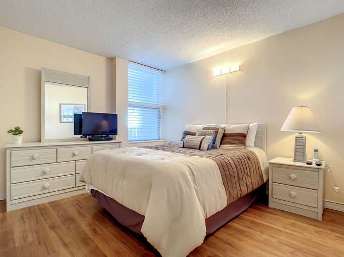 Beige Bedroom With Bed, Dresser, And TV, Bathed In Bright Light