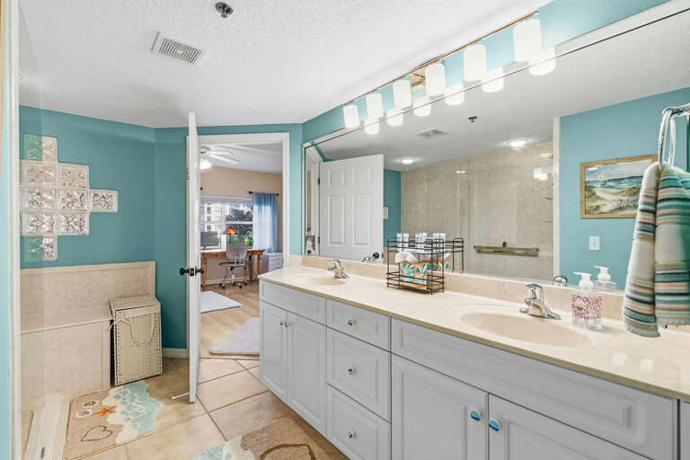Bright ensuite bathroom with dual sinks, large mirror, and walk-in shower. Coastal tones and ample