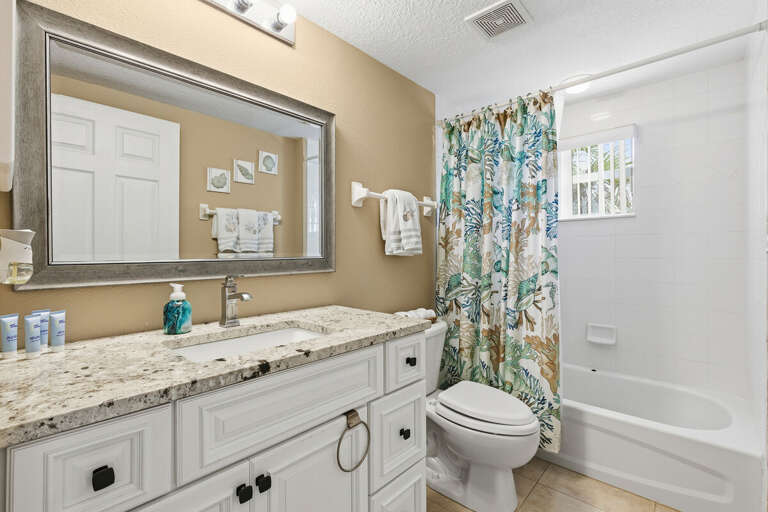Fresh and inviting bathroom with tub/shower combo, granite vanity, and coastal accents. Perfect for your beach stay, offering comfort and convenience for guests after a relaxing day by the ocean.