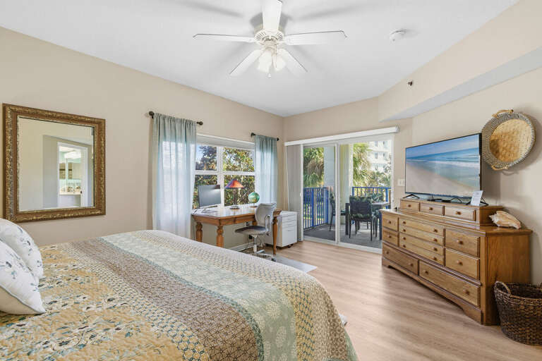 Spacious master bedroom with cozy bedding, TV, workspace, and private balcony access. Enjoy indoor-outdoor living during your beach stay, perfect for relaxing after a day by the ocean.