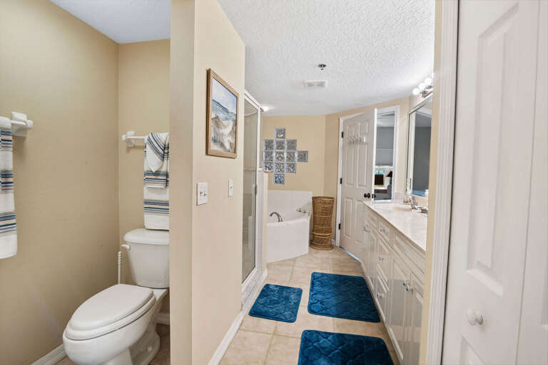 Unwind in this bright ensuite bathroom featuring a double vanity, glass shower, and soaking tub. A comfortable, spa-like space to refresh after a sun-filled day enjoying your beach stay getaway.