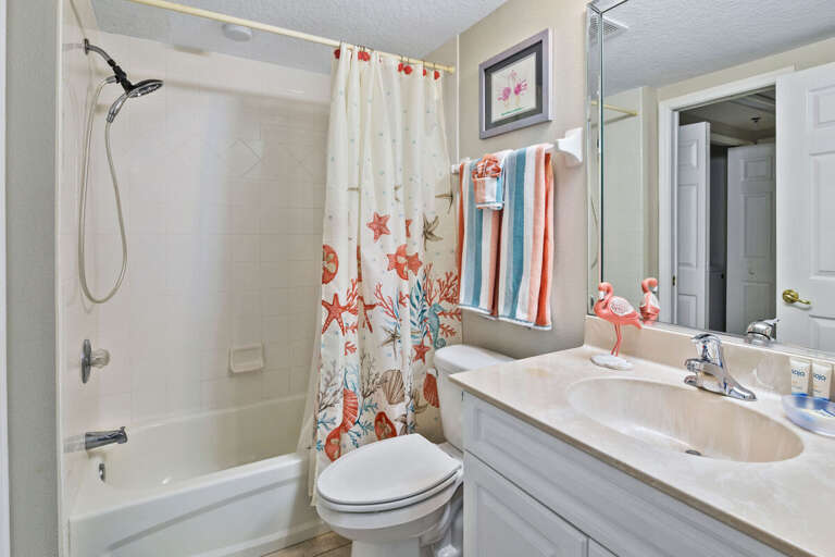 Freshen up during your beach stay in this bright guest bathroom featuring a tub and shower combo, coastal décor, and plush towels. A convenient space to unwind after a sunny day by the shore.