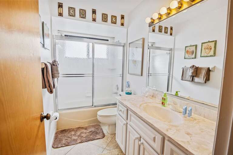 Clean, well-lit bathroom with large vanity, shower-tub combo, and fresh towels. Perfect for