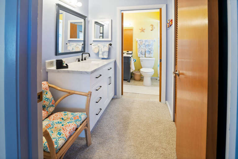 This beach stay features a bright vanity area with modern finishes and coastal accents, leading to a private bath. Enjoy added space and convenience to get ready after a relaxing day at the beach.