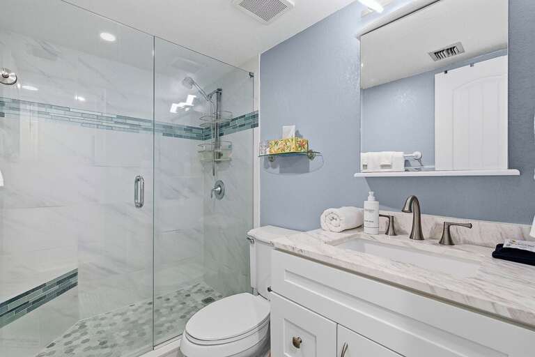 Refresh in this clean, modern bathroom during your beach stay, featuring a glass walk-in shower, sleek finishes, and bright coastal style—perfect for unwinding after a day by the ocean.