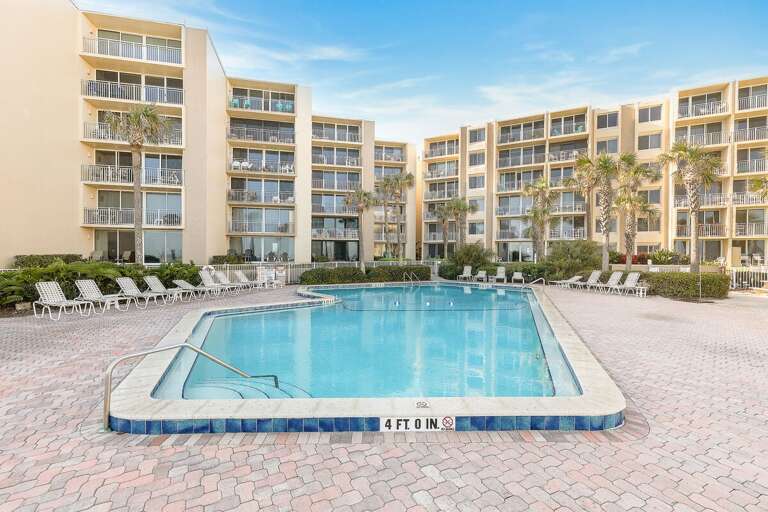 Spend sunny beach days relaxing by the spacious resort pool, complete with lounge seating, palm trees, and plenty of room to unwind—a refreshing amenity to enjoy throughout your coastal beach stay.